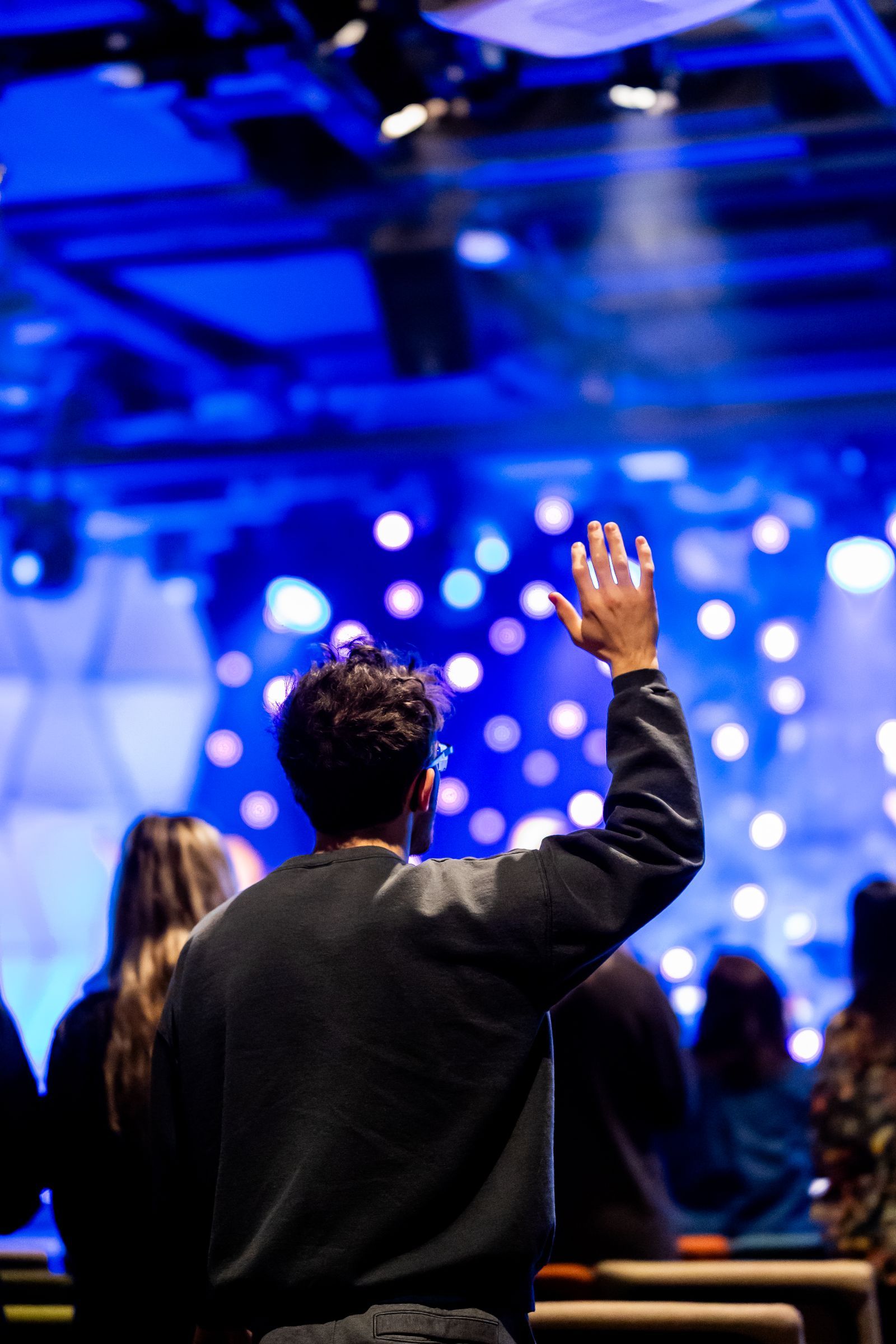 Worshippers with hands raised under blue lights